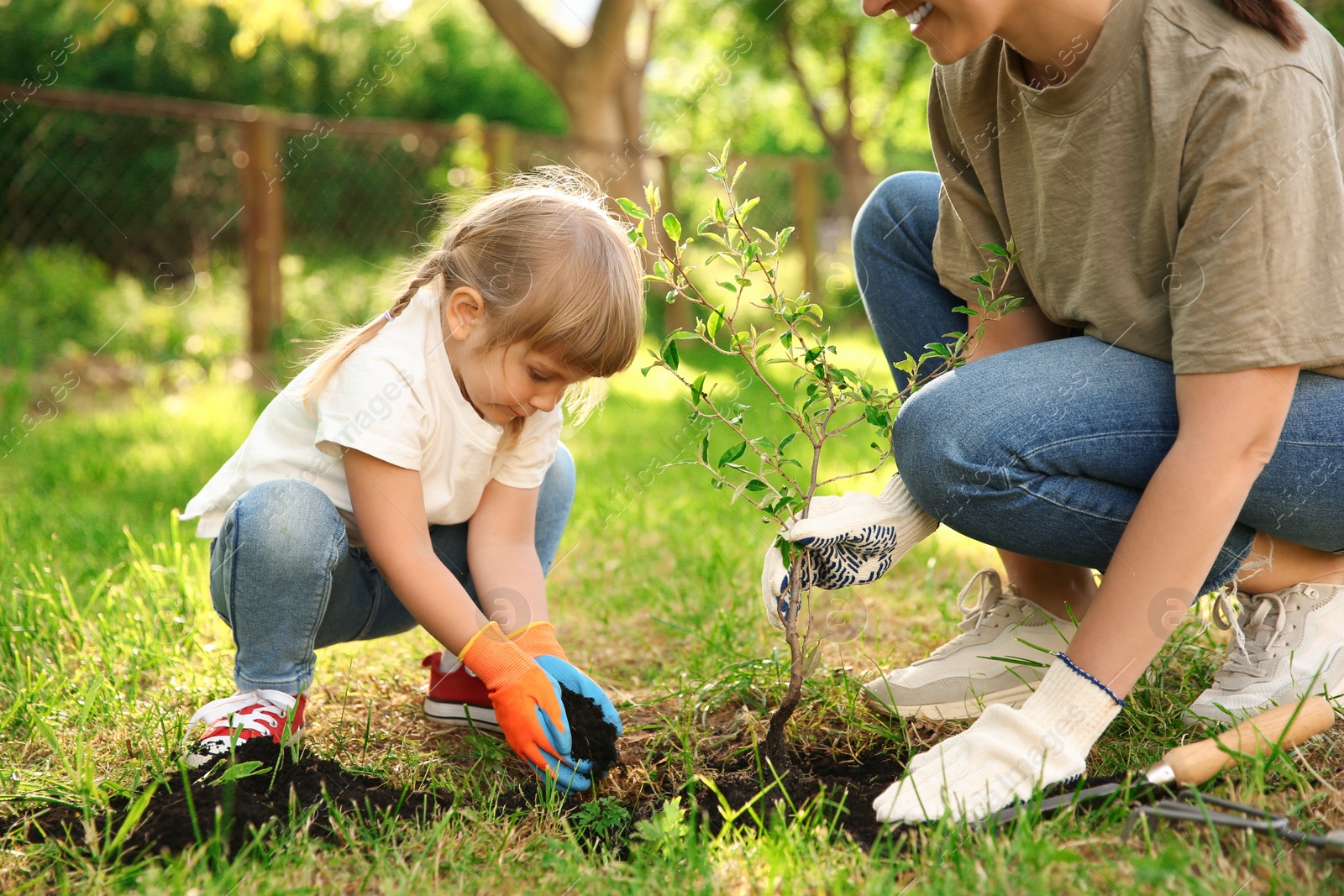 Photo of Mother and her daughter planting tree together in garden