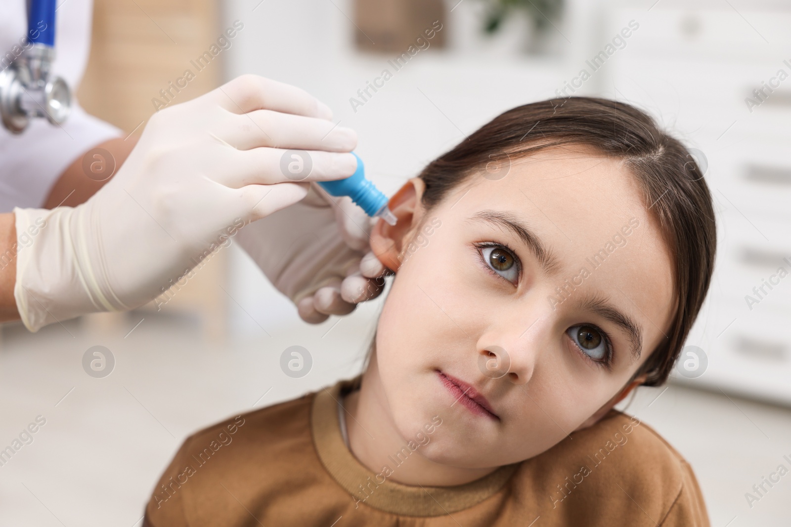 Photo of Doctor applying medical drops into girl's ear indoors