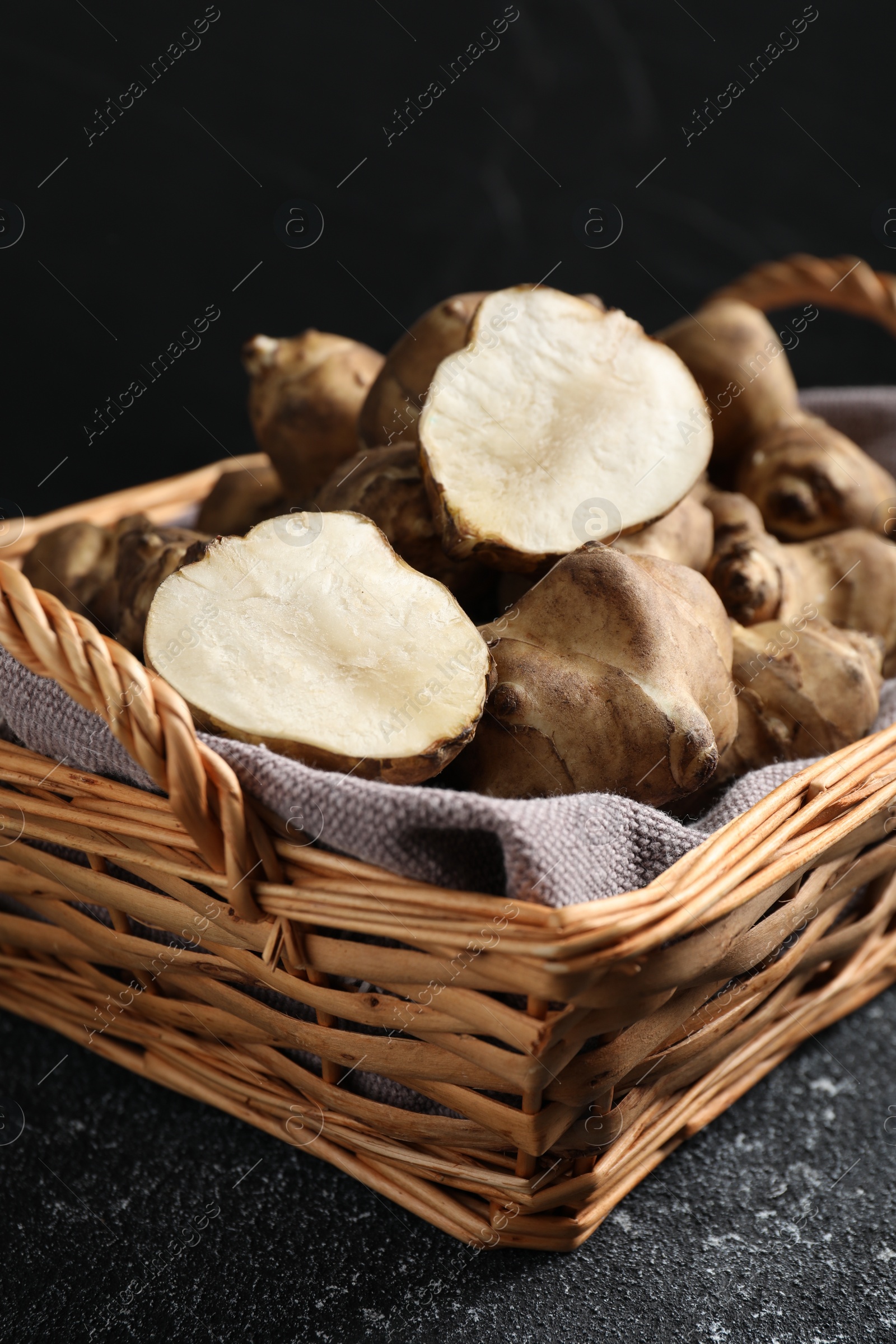 Photo of Wicker basket with many Jerusalem artichokes on light grey table