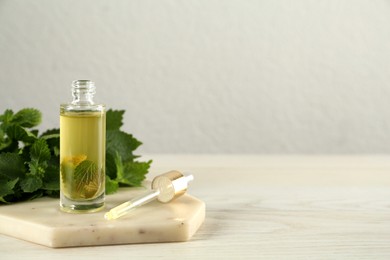 Photo of Glass bottle of nettle oil with dropper and leaves on white table, space for text