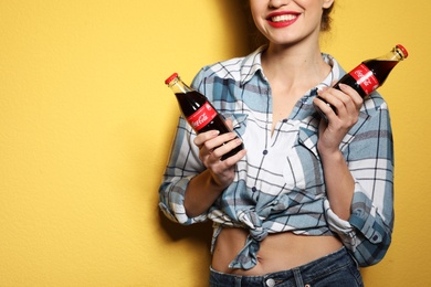 Photo of MYKOLAIV, UKRAINE - NOVEMBER 28, 2018: Young woman with bottles of Coca-Cola on color background, closeup. Space for text