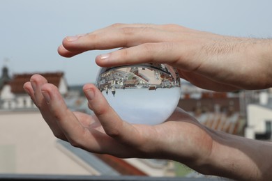 Photo of View of beautiful city street, overturned reflection. Man holding crystal ball outdoors, closeup