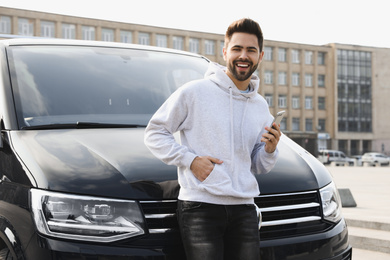 Photo of Handsome young man with smartphone near modern car outdoors