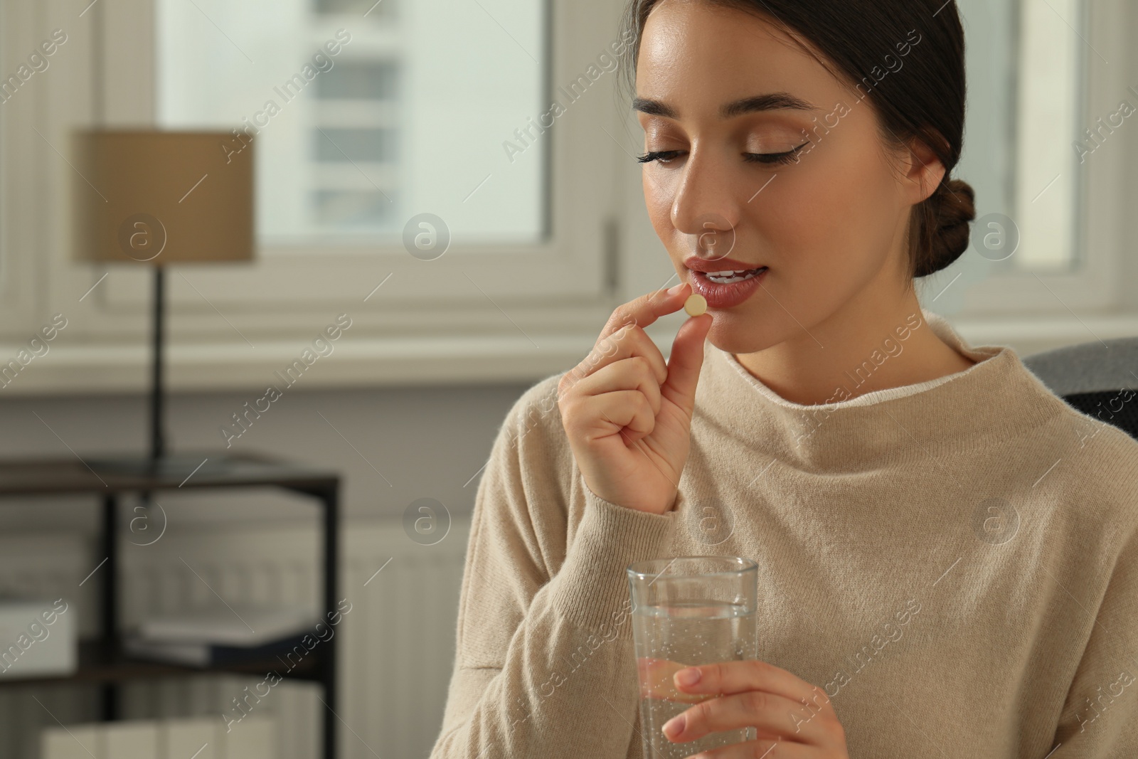 Photo of Young woman with glass of water taking dietary supplement pill indoors, space for text
