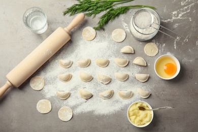 Photo of Flat lay composition with raw dumplings and ingredients on grey background. Process of cooking