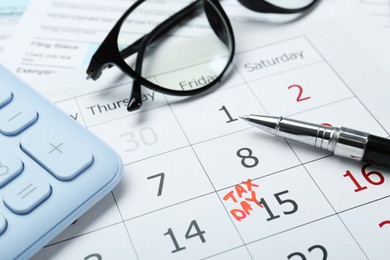 Photo of Tax day. Calendar with date reminder, pen, glasses and calculator on table, closeup