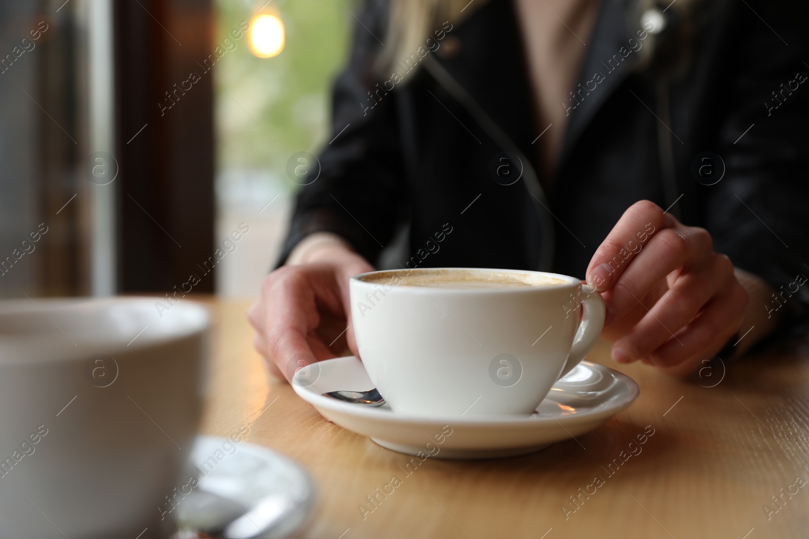 Photo of Young woman with cup of coffee at table in morning, closeup