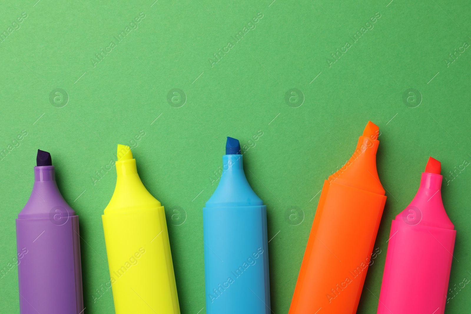 Photo of Bright color markers on green background, flat lay. Space for text