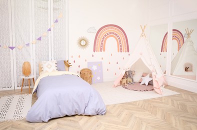 Photo of Stylish room with comfortable bed and teepee tent for kids. Interior design