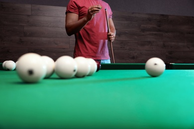 Young man chalking cue near billiard table indoors, closeup