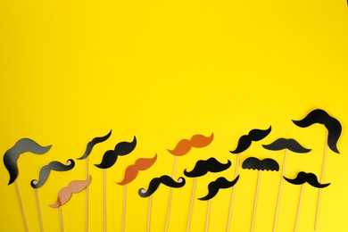 Photo of Fake paper mustaches with sticks on yellow background, flat lay. Space for text