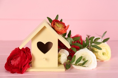 Stylish bird house and fresh eustomas on pink wooden table