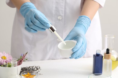 Photo of Scientist developing cosmetic oil at white table, closeup