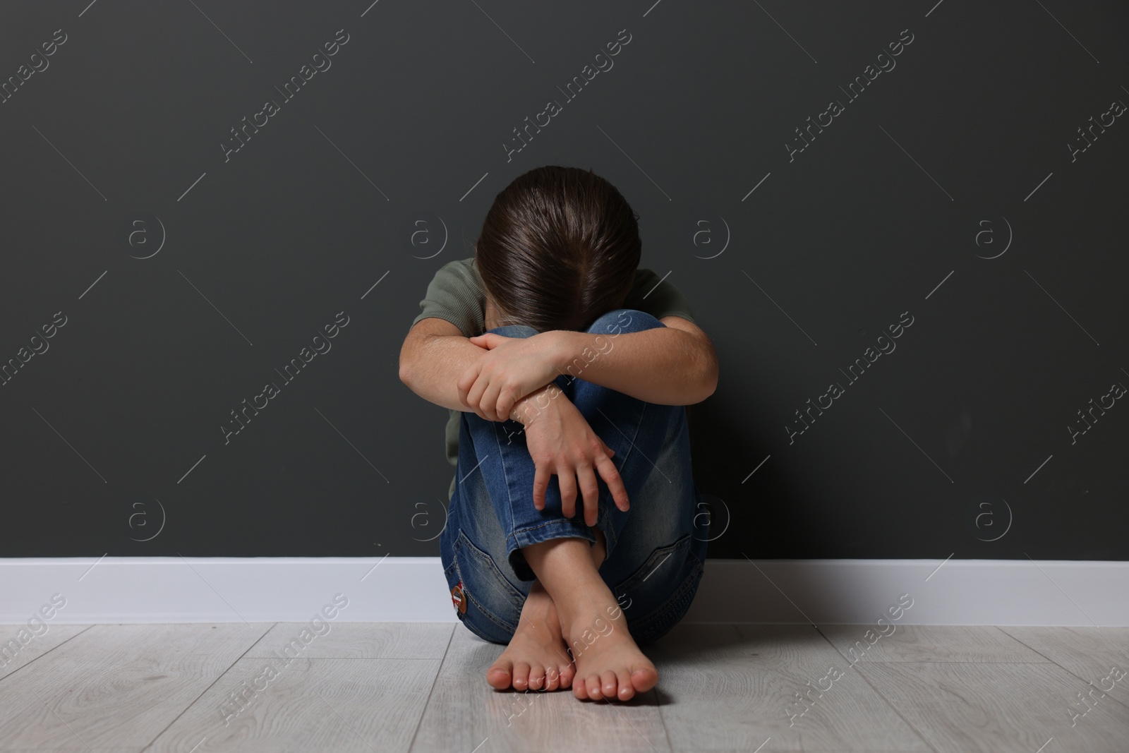 Photo of Child abuse. Upset girl sitting on floor near grey wall