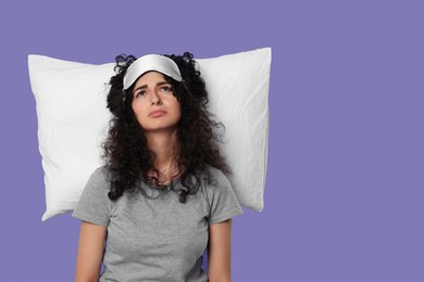 Tired young woman with sleep mask and pillow on purple background, space for text. Insomnia problem