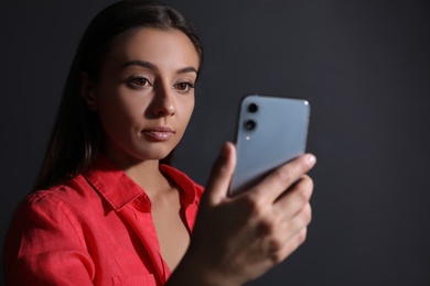 Young woman unlocking smartphone with facial scanner on black background. Biometric verification