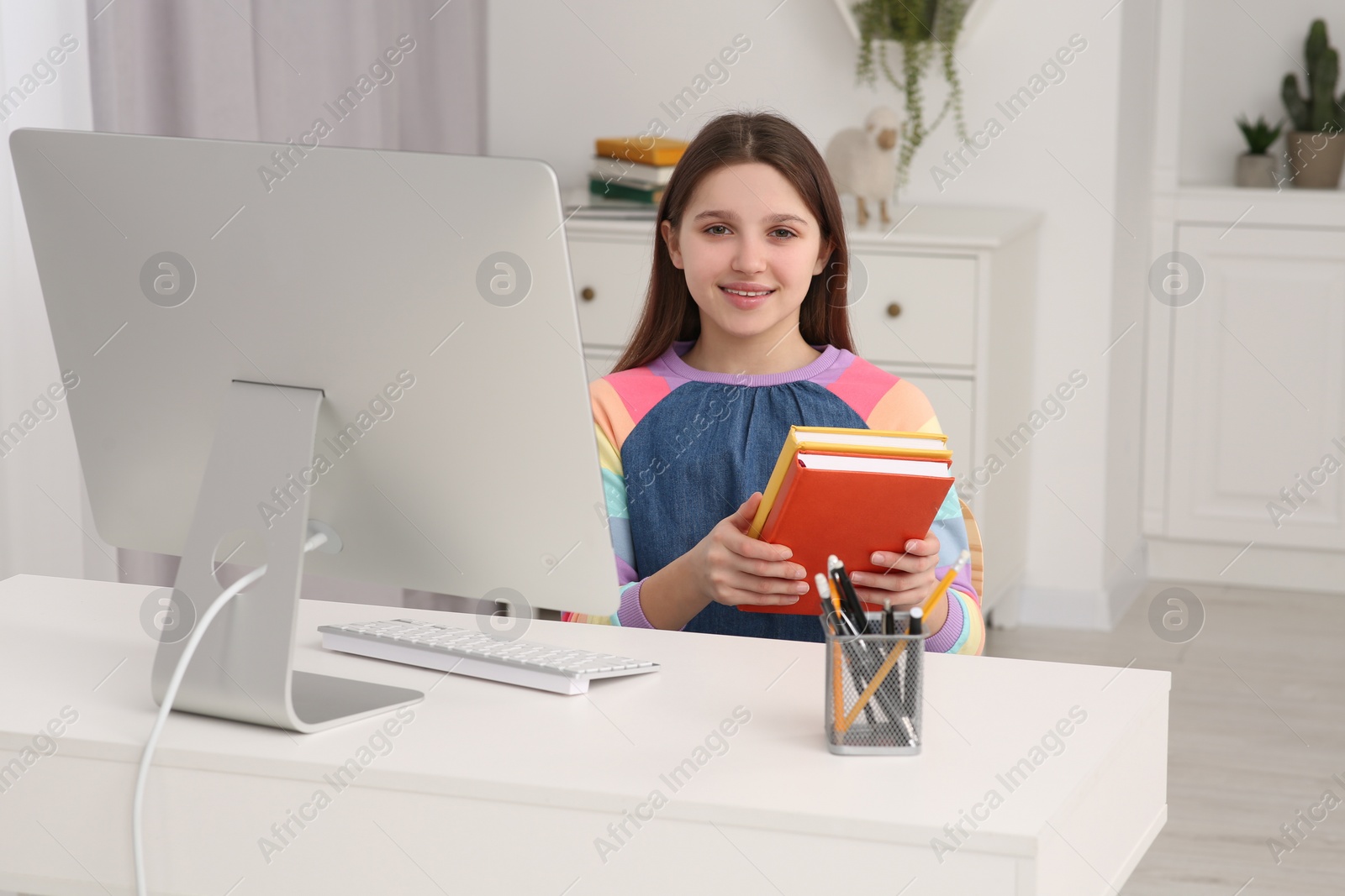 Photo of Cute girl with books using computer at desk in room. Home workplace