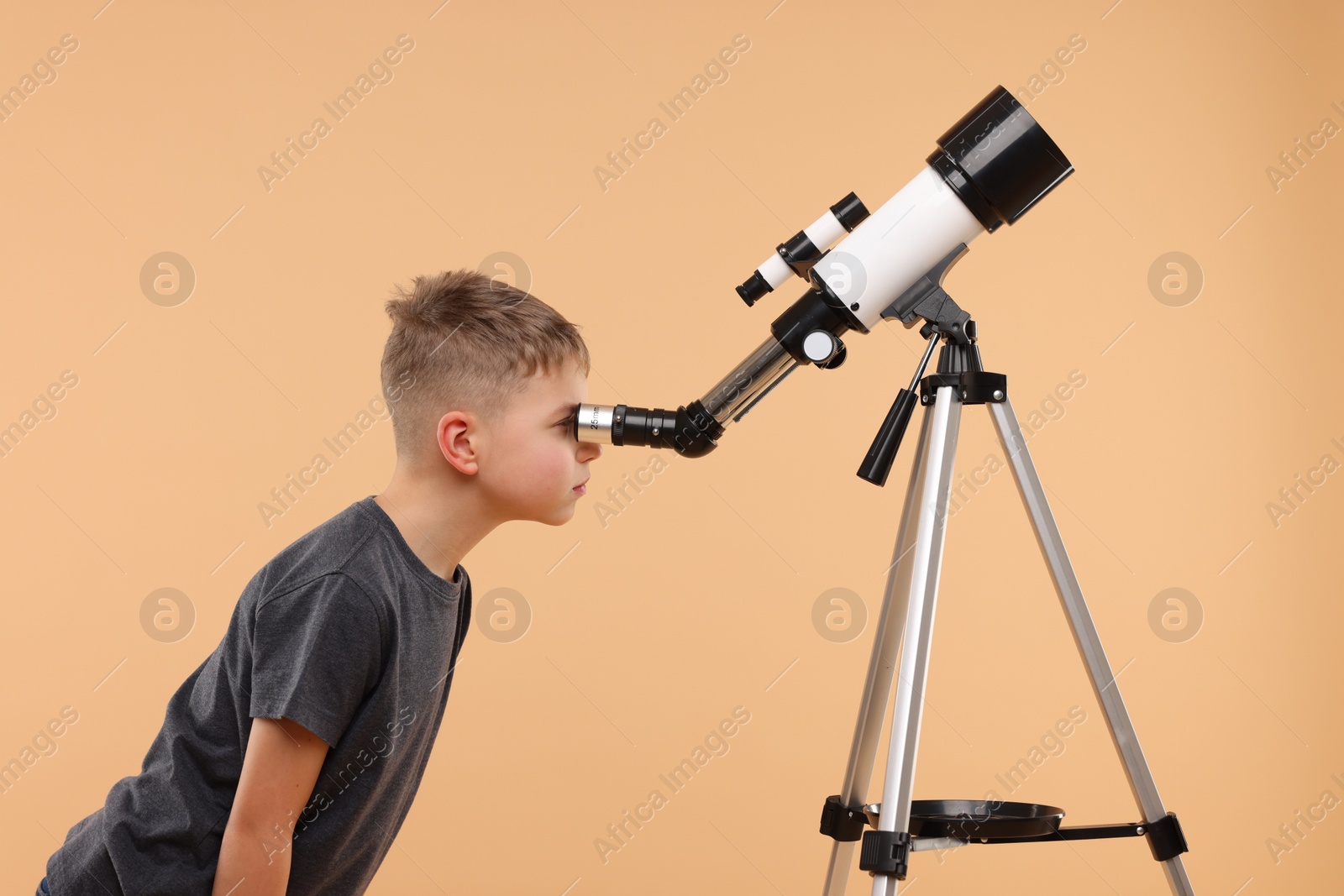 Photo of Little boy looking at stars through telescope on beige background