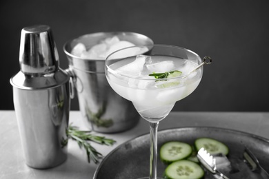 Photo of Glass of martini with cucumber, shaker and ice bucket on table against dark background. Space for text