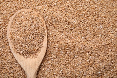 Photo of Wooden spoon with dry wheat groats, top view. Space for text