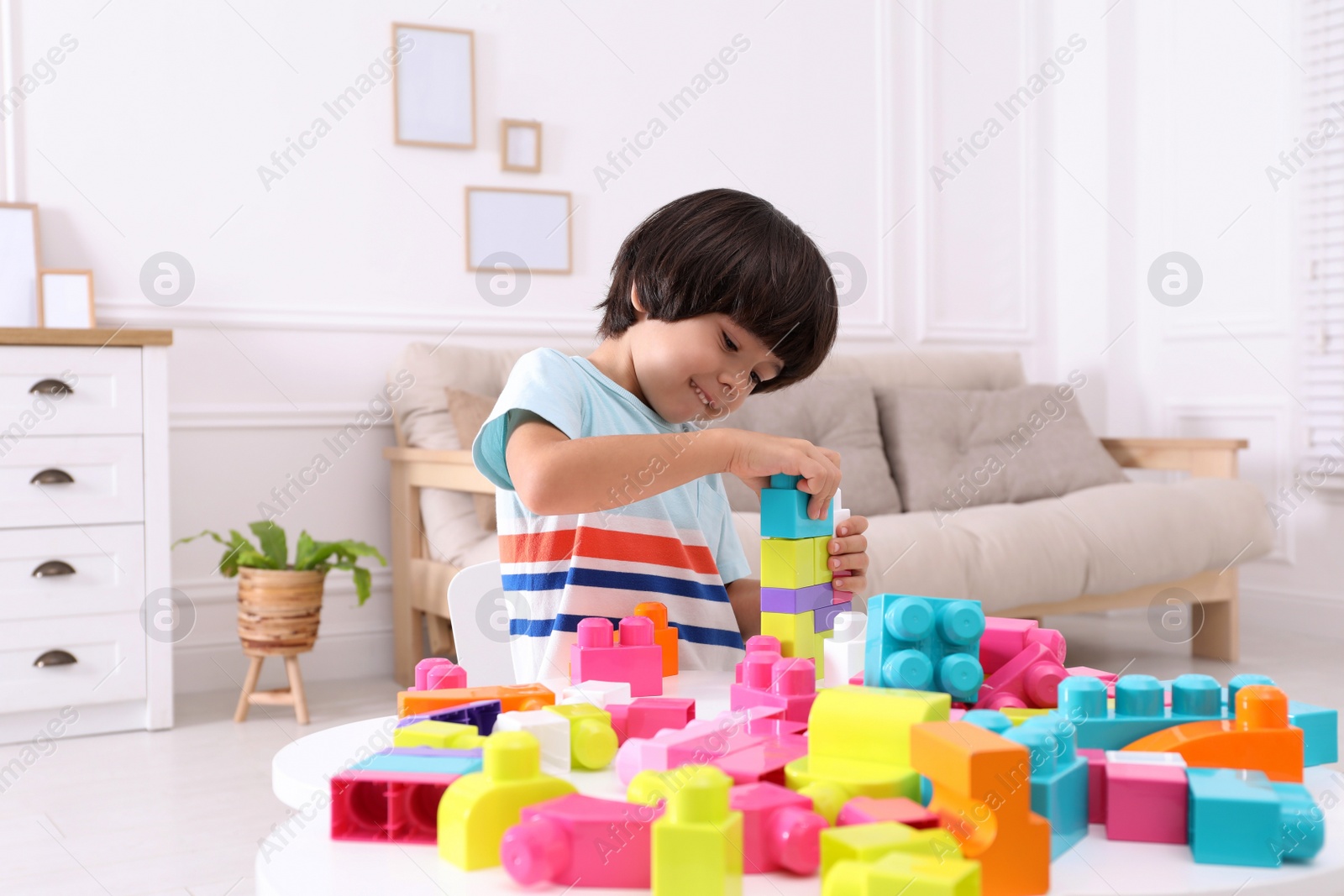 Photo of Cute little boy playing with colorful building blocks at table in living room