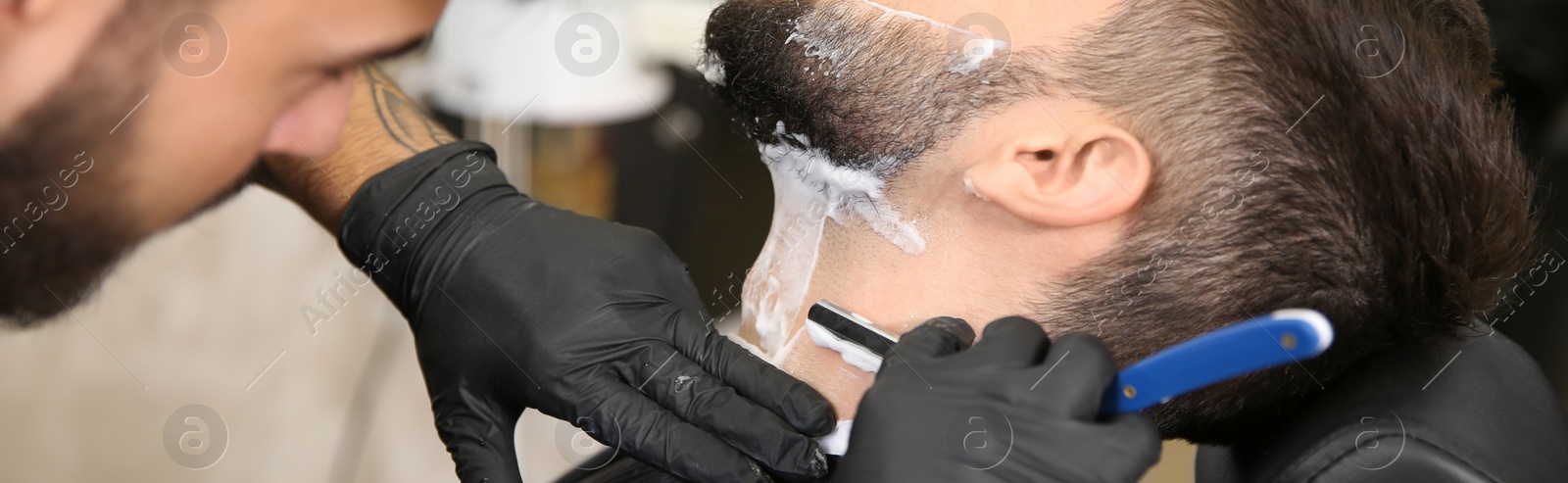 Image of Professional hairdresser shaving client with straight razor in barbershop, closeup. Banner design