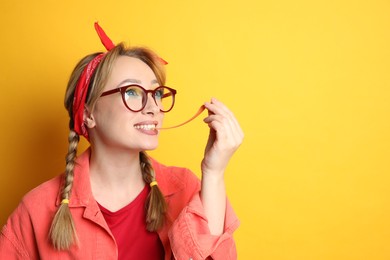 Photo of Fashionable young woman with braids and bright makeup chewing bubblegum on yellow background, space for text