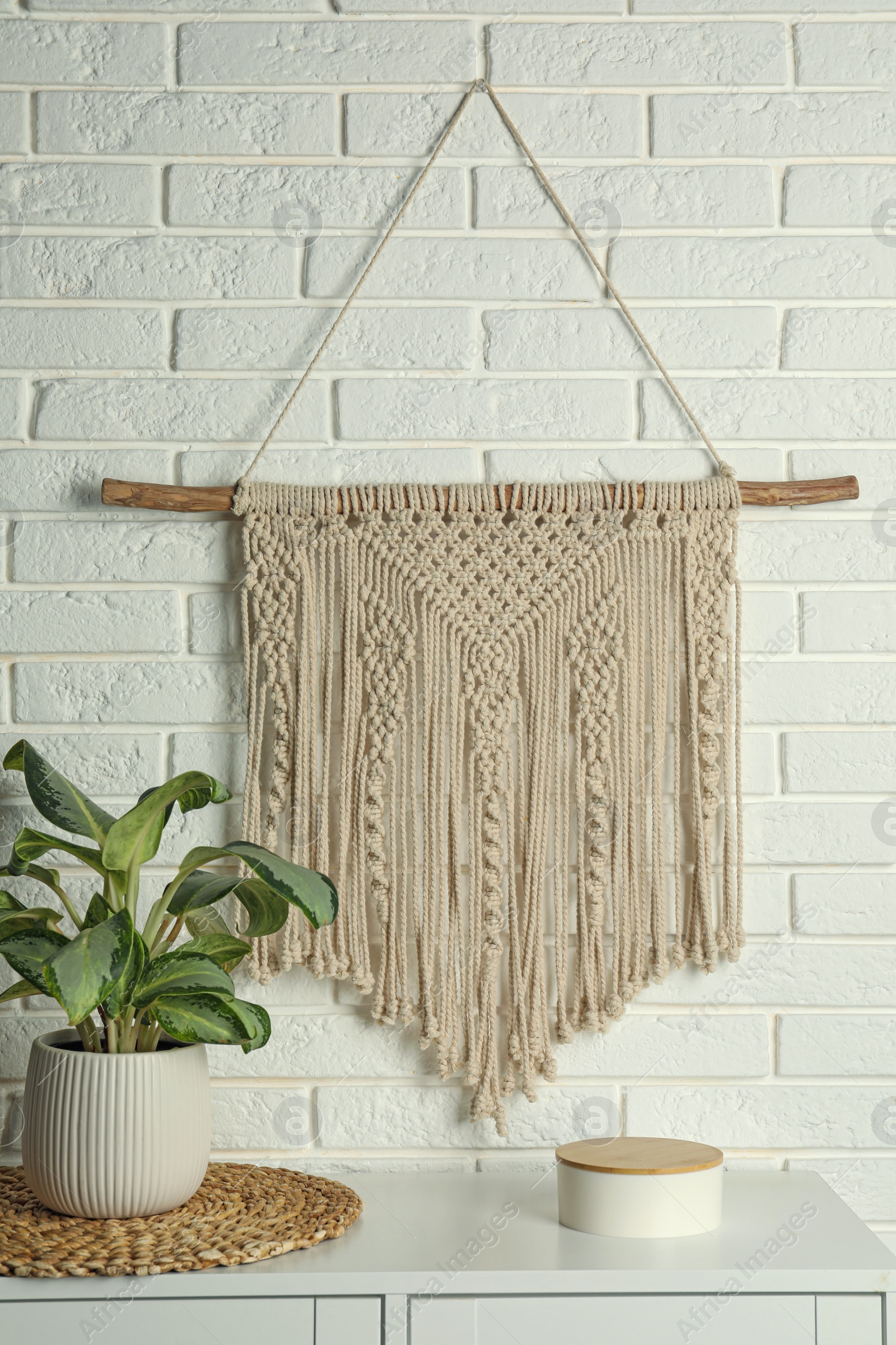 Photo of Beautiful macrame hanging on white brick wall in room. Decorative element