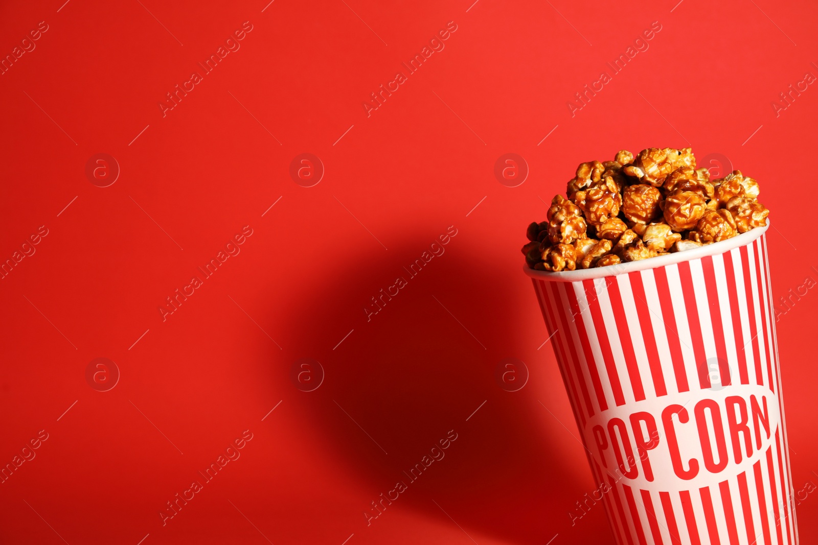 Photo of Caramel popcorn in paper cup on color background. Space for text