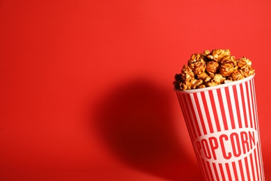 Photo of Caramel popcorn in paper cup on color background. Space for text