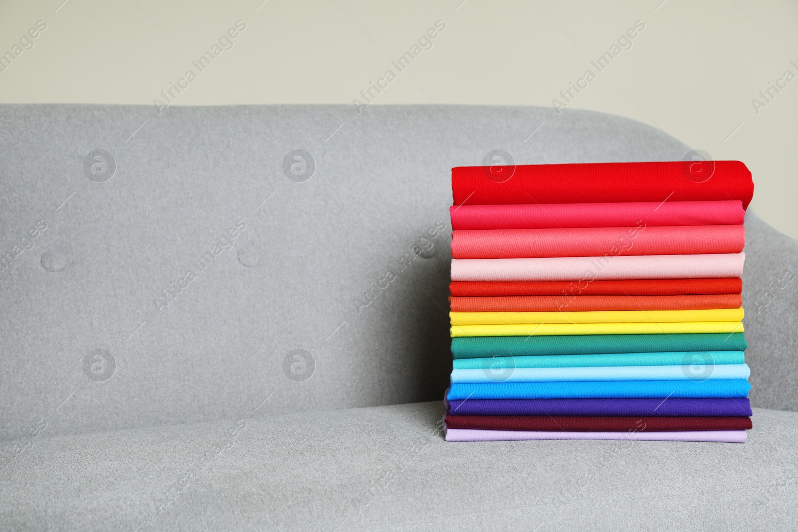 Photo of Pile of bright t-shirts on sofa indoors