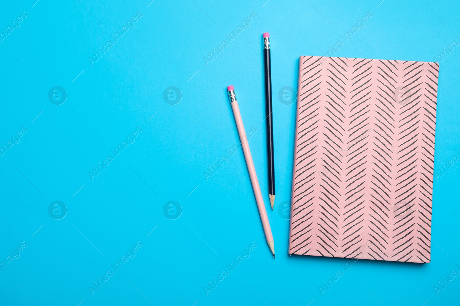 Photo of Pink notebook and pencils on light blue background, flat lay. Space for text