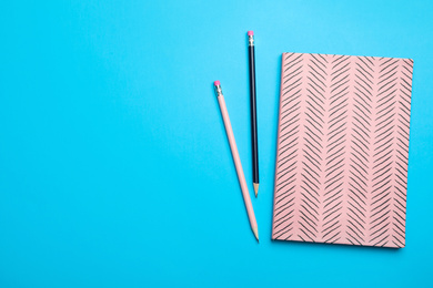 Photo of Pink notebook and pencils on light blue background, flat lay. Space for text