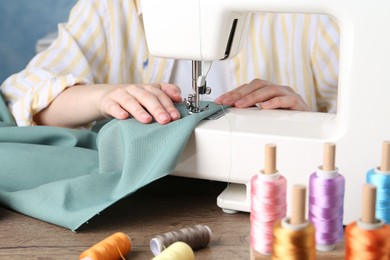 Photo of Seamstress working with sewing machine at wooden table indoors, closeup