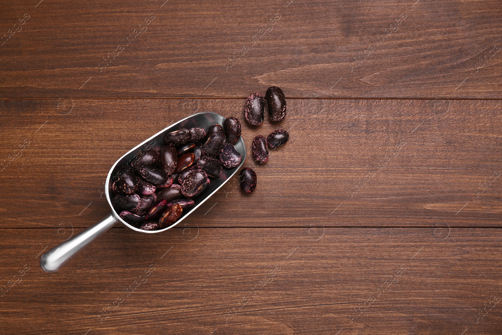 Photo of Metal scoop with dry kidney beans on wooden table, flat lay. Space for text