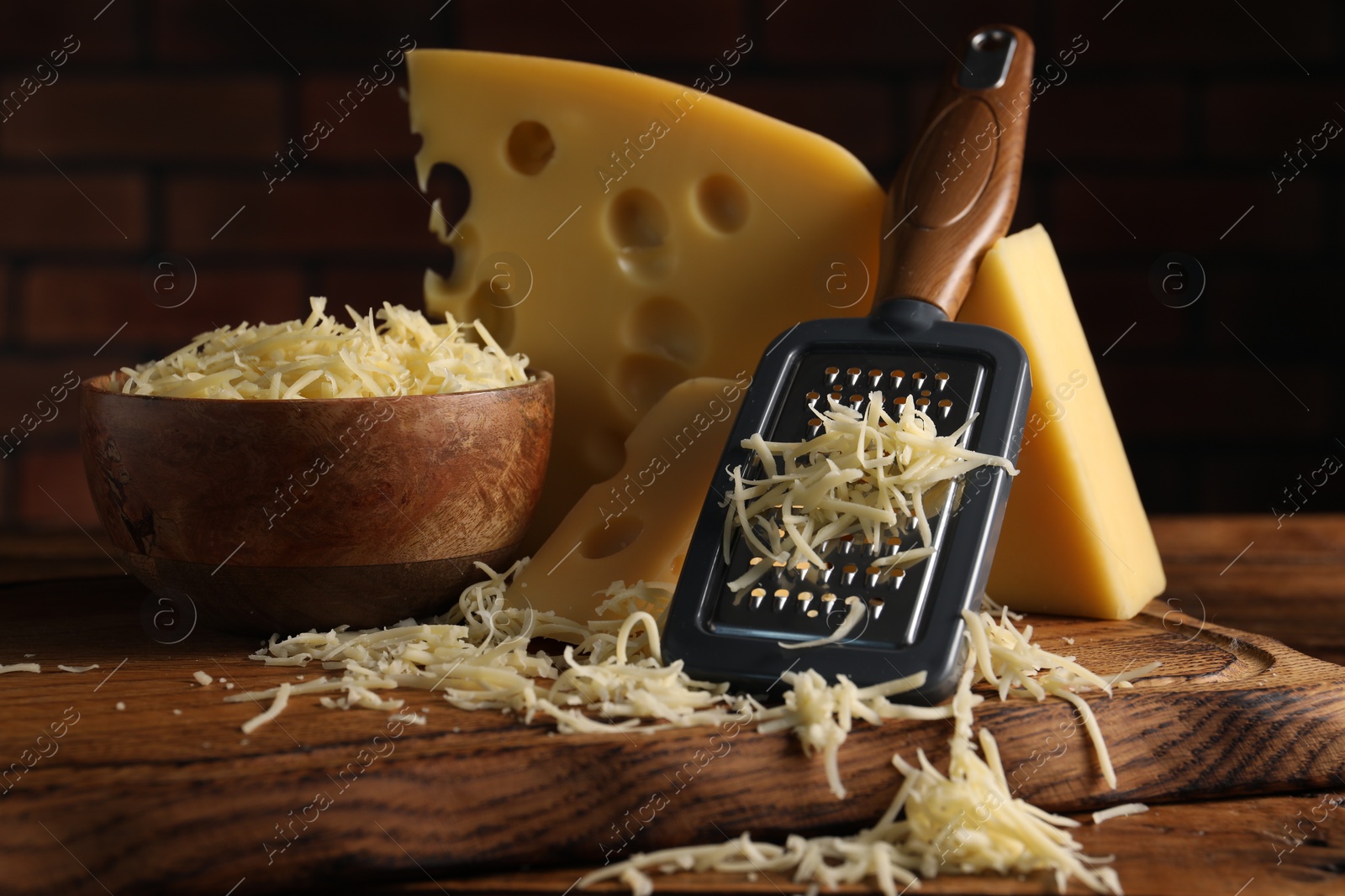 Photo of Grated, cut cheese and grater on wooden table, closeup