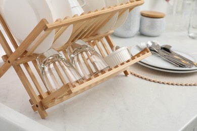 Photo of Drying rack with clean dishes on light marble countertop in kitchen, closeup