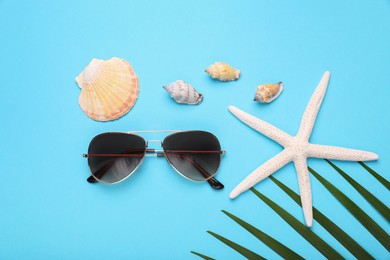 Stylish sunglasses, starfish and seashells on light blue background, flat lay