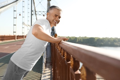 Handsome mature man in sportswear doing exercise on bridge. Healthy lifestyle