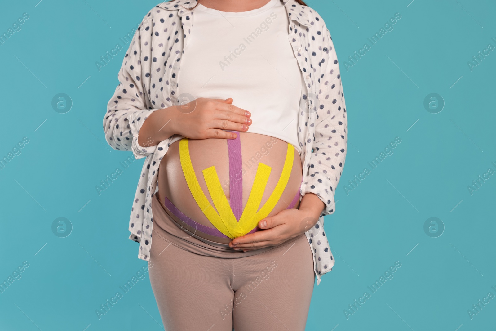 Photo of Pregnant woman with kinesio tapes on her belly against light blue background, closeup
