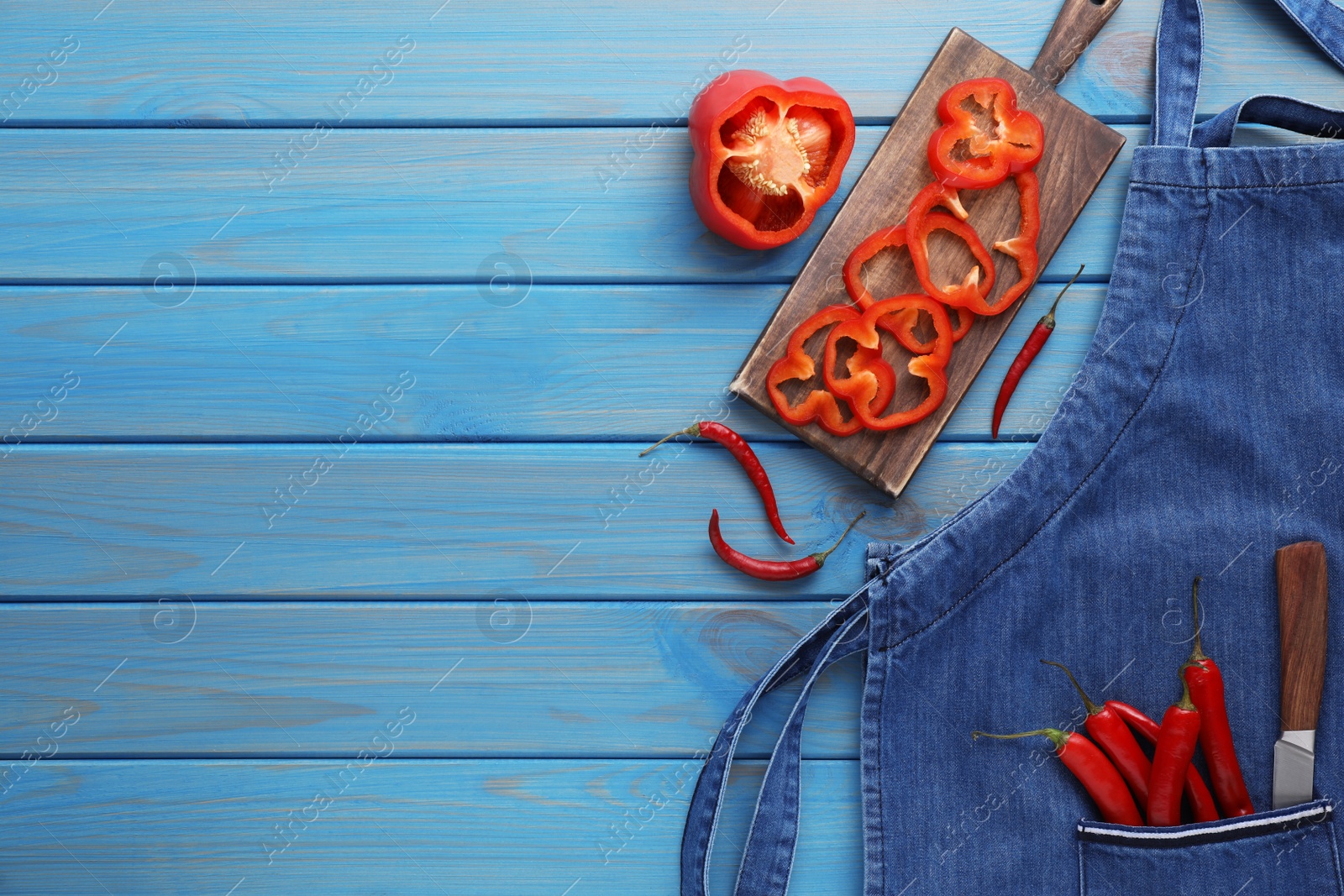 Photo of Flat lay composition with denim apron and fresh peppers on light blue wooden table. Space for text