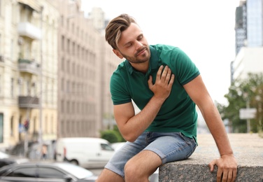 Photo of Young man having heart attack on city street. Space for text