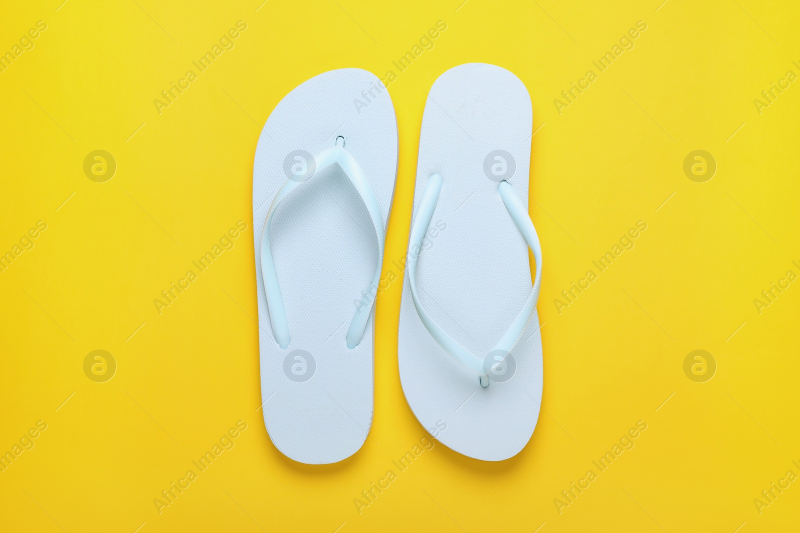 Photo of Stylish white flip flops on yellow background, top view