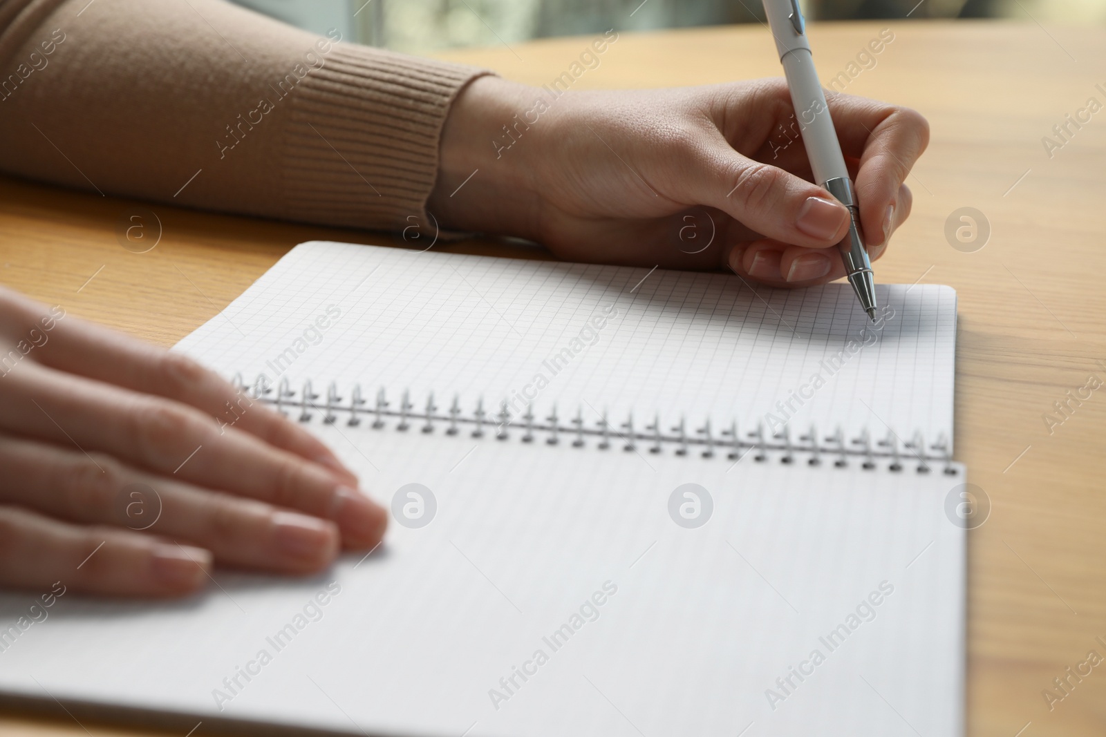 Photo of Left-handed woman writing in notebook at wooden desk, closeup