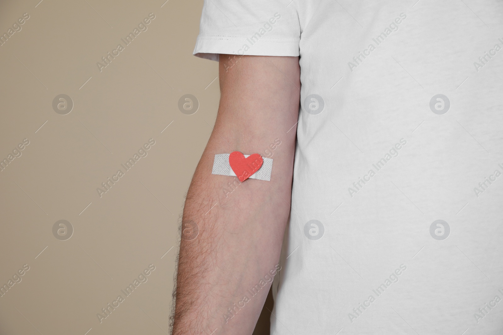 Photo of Blood donation concept. Man with adhesive plaster on arm against beige background, closeup. Space for text