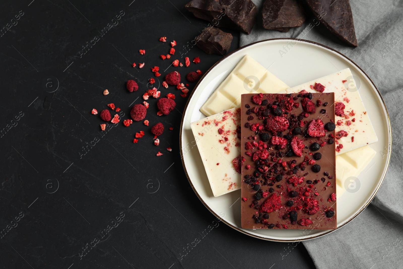 Photo of Chocolate bars with freeze dried fruits on black table, flat lay. Space for text