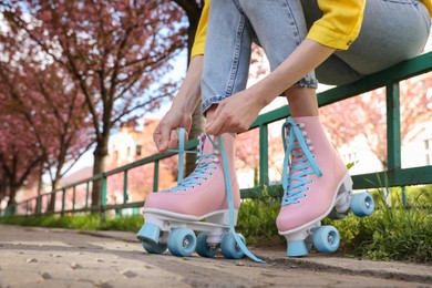 Photo of Young woman putting on roller skates outdoors, closeup