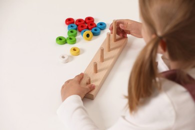 Photo of Little girl playing with stacking and counting game at white table indoors, closeup. Child's toy