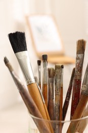 Photo of Glass holder with different paintbrushes indoors, closeup