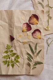 Sheets of paper with dried flowers and leaves on white fabric, flat lay